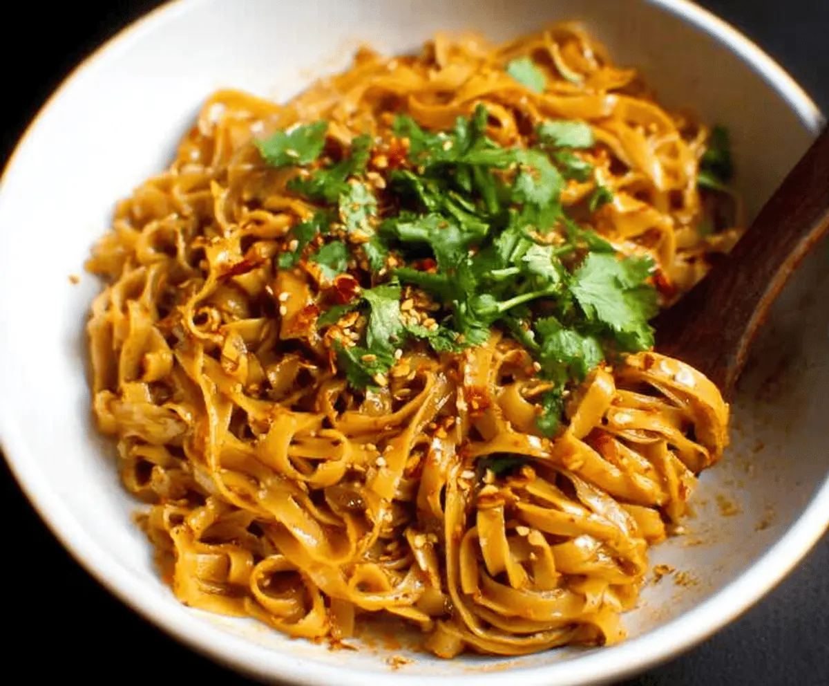 A vibrant bowl of spicy chili garlic noodles garnished with chopped green onions and red chili flakes, showcasing the flavorful, savory Asian-inspired dish.