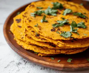 Freshly made sweet potato tortillas stacked on a wooden surface, showcasing their vibrant orange color and soft texture, perfect for healthy wraps and tacos.