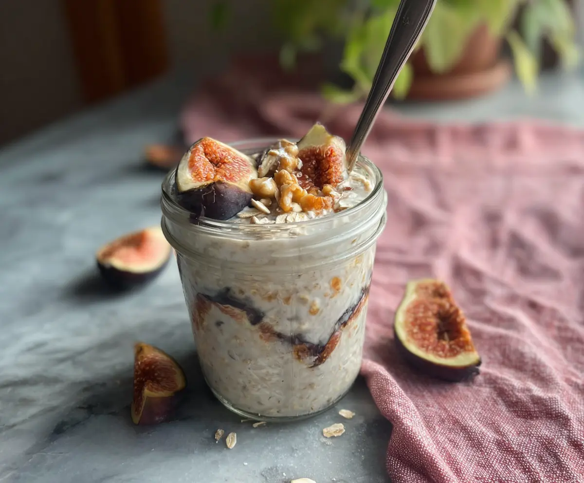 Healthy Coconut Fig Overnight Oats in a glass jar with fresh figs and shredded coconut on a wooden table.